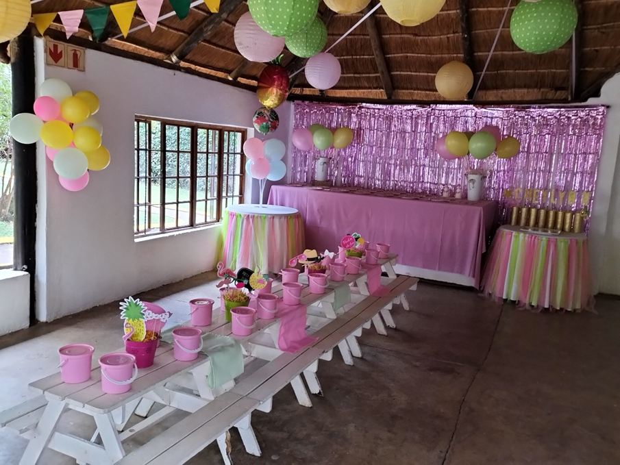 Long tables set with pink party packs under balloon d&eacute;cor